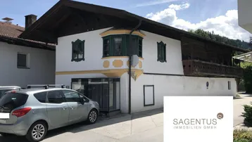 Traditionelles Gebäude mit weißer Fassade, Holzbalkonen und einem Erker, teilweise verdeckt durch ein Auto.