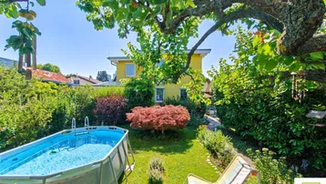 Sonnige Gartenoase mit Aufstellpool, Liegestuhl und üppiger Bepflanzung hinter dem Haus.