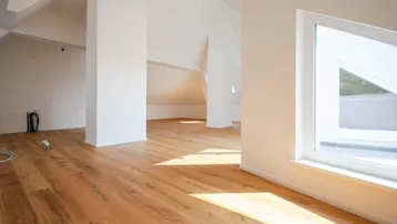 Heller, offener Raum im Dachgeschoss mit Holzboden und großen Fenstern, bereit für die Einrichtung.