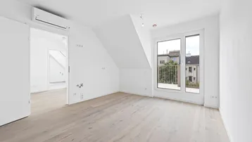 Helles Zimmer mit Holzboden, Dachschräge und Zugang zu einem kleinen Balkon. Klimaanlage ist ebenfalls vorhanden.