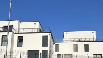 Moderne weiße Gebäude mit Flachdächern und Balkonen unter klarem blauem Himmel.