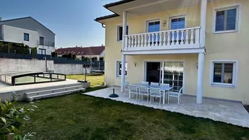 Hausfassade mit sonnigem Garten, Terrasse und Balkon, ideal für Entspannung im Freien.