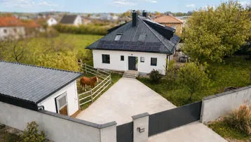 Luftaufnahme eines modernen Einfamilienhauses mit Solaranlage, großem Grundstück und Pferd auf der Weide.