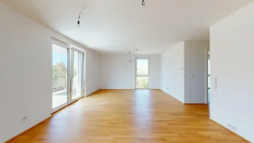 Helles, unmöbliertes Wohnzimmer mit Holzboden und Zugang zu einem Balkon.