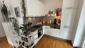 Helle Küche mit weißen Schränken, Holzboden und integrierten Geräten in einem modernen Stil.