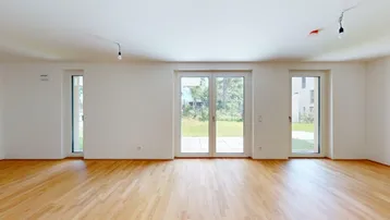 Helles Wohnzimmer mit großen Fenstern, Holzboden und Zugang zum Garten.