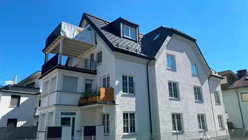 Modernes Mehrfamilienhaus mit weißer Fassade, Satteldach und Balkonen in sonniger Lage.