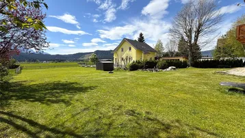 Weitläufiger grüner Garten mit dem Wohnhaus im Hintergrund und Blick auf die umliegende Landschaft.