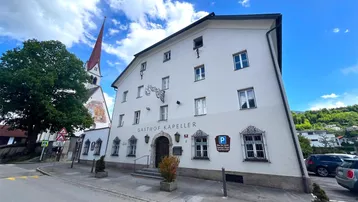Weißes historisches Gebäude mit rotem Kirchturm im Hintergrund unter blauem Himmel.