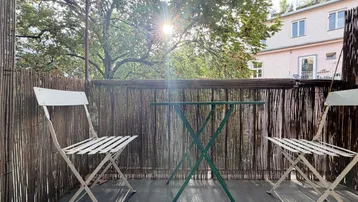 Sonnige Loggia mit Bambusabtrennung, zwei Stühlen und einem kleinen Tisch, ideal zum Entspannen.