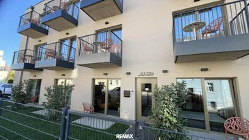 Moderne Gebäudefassade mit mehreren Balkonen, die mit Tischen und Stühlen ausgestattet sind.