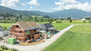 Neubau eines Einfamilienhauses im Rohbau mit Dachstuhl in ländlicher Umgebung und Bergblick.