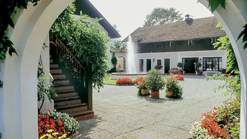 Sonniger Innenhof mit Springbrunnen, Blumenbeeten und traditioneller Architektur.
