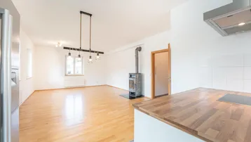 Heller offener Wohnbereich mit Holzboden, Kaminofen und Blick auf die moderne Küche.