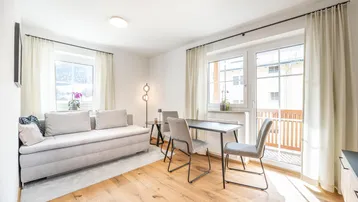 Helles Wohn- und Esszimmer mit Holzboden, bequemer Couch und Zugang zum Balkon.