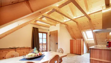 Rustikaler Essbereich mit Holztisch, Dachschrägen und sichtbaren Holzbalken, kombiniert mit einer kleinen Küchenzeile.