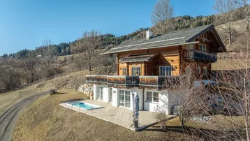 Traditionelles Holzhaus im Chalet-Stil mit Terrasse, Whirlpool und Bergblick in sonniger Hanglage.