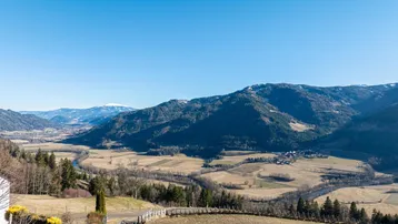 Panoramablick auf die weite Berglandschaft mit Tälern und Wäldern unter blauem Himmel.