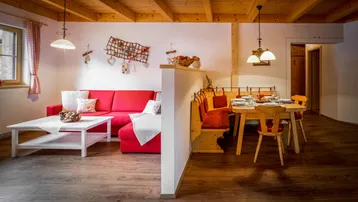 Helles Wohn- und Esszimmer im alpinen Stil mit Holzbalkendecke und gemütlichem roten Sofa.