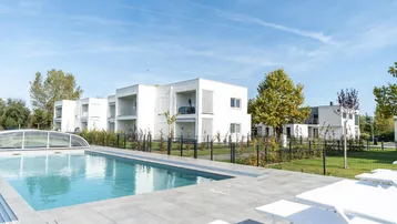 Moderne Wohngebäude mit Gemeinschaftspool und Liegewiese unter blauem Himmel.