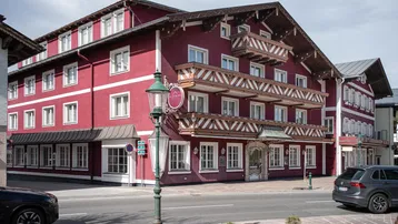 Traditionelles Gebäude mit roter Fassade, weißen Fenstern und verzierten Holzbalkonen an einer Straße.
