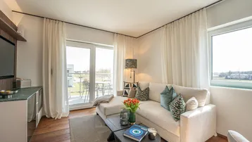 Helles Wohnzimmer mit modernem Sofa, Holzboden und Zugang zum sonnigen Balkon.