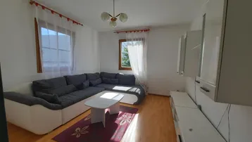 Helles Wohnzimmer mit großem Ecksofa, Holzboden und weißen Schränken, durchflutet von natürlichem Licht.