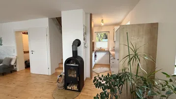 Gemütlicher Wohnbereich mit einem modernen Holzofen, Holzboden und Blick zur Küche.