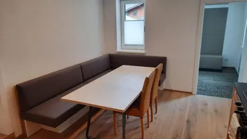 Gemütlicher Essbereich mit Eckbank und Holzboden, der in einen weiteren Raum führt.
