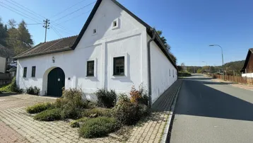 Weißes Landhaus mit traditioneller Architektur und grünen Fensterläden an einer ruhigen Straße.