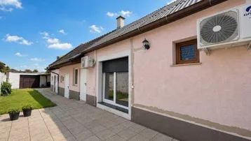 Seitenansicht eines Hauses mit gepflastertem Weg, kleiner Rasenfläche und Klimaanlage an der Fassade.