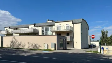 Modernes Mehrfamilienhaus mit hellbeiger Fassade, großen Fenstern und mehreren Balkonen unter blauem Himmel.