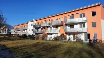 Modernes Mehrfamilienhaus mit orangefarbener Fassade, Balkonen und Blick auf die Berge.
