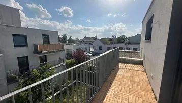 Heller Balkon mit Holzbodenfliesen und Blick auf die umliegenden Gebäude und Bäume.