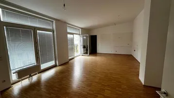 Geräumiger, leerer Wohnbereich mit Parkettboden, großen Fenstern und Zugang zu einem Balkon.