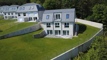 Neubau-Doppelhaushälfte mit großem Garten und moderner Architektur in grüner Umgebung.