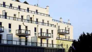 Moderne Wohnfassade mit mehreren Balkonen und großen Fenstern unter klarem Himmel.