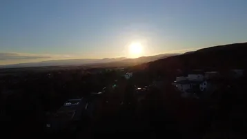 Malerischer Sonnenuntergang über einer weiten Landschaft mit entfernten Bergen und Siedlungsgebieten.