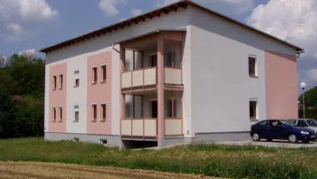 Neues Mehrfamilienhaus mit moderner Architektur, weiß-rosa Fassade, Balkonen und ländlichem Ausblick.