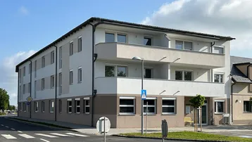 Modernes Mehrfamilienhaus mit heller Fassade, Balkonen und großen Fenstern an einer Straßenecke.