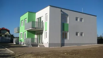 Modernes Mehrfamilienhaus mit grünen und grauen Fassaden, Balkonen und Flachdach in einem Neubaugebiet.