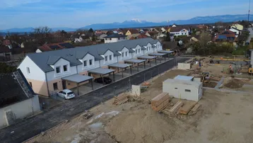 Luftaufnahme einer Reihe von Neubauhäusern mit Carports und einer Baustelle im Vordergrund.