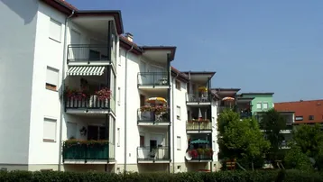 Mehrfamilienhaus mit weißen Fassaden, mehreren Loggien und einem kleinen Spielplatz im Vorgarten.
