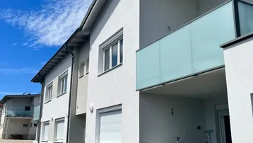 Moderne Wohngebäude mit weißer Fassade, Glasbalkonen und Rollläden unter blauem Himmel.