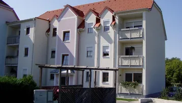 Mehrstöckiges Wohngebäude mit hellen Fassaden, roten Ziegeldächern und mehreren Balkonen.