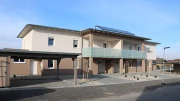 Neubau-Wohngebäude mit modernen Balkonen, Carports und Photovoltaikanlage auf dem Dach.