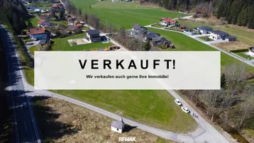 Luftaufnahme einer ländlichen Wohngegend mit Häusern, Feldern und Wald, inklusive Verkaufsanzeige.