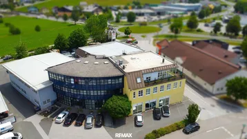 Luftaufnahme eines modernen Bürogebäudes mit umliegenden Grünflächen und Parkplätzen in einer städtischen Umgebung.