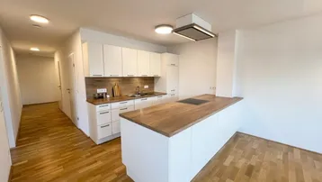 Moderne Einbauküche mit weißen Schränken, Holztheke und integriertem Kochfeld, offen zum Wohnbereich.
