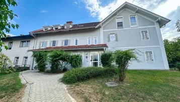 Großes Wohngebäude mit mehreren Fenstern, Dachgauben und einem gepflasterten Zugangsweg.